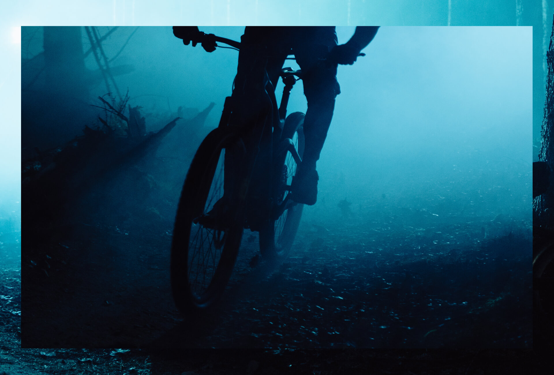 Mann fährt Mountainbike im dunklen Wald mit blauen Lichtern im HIntergrund