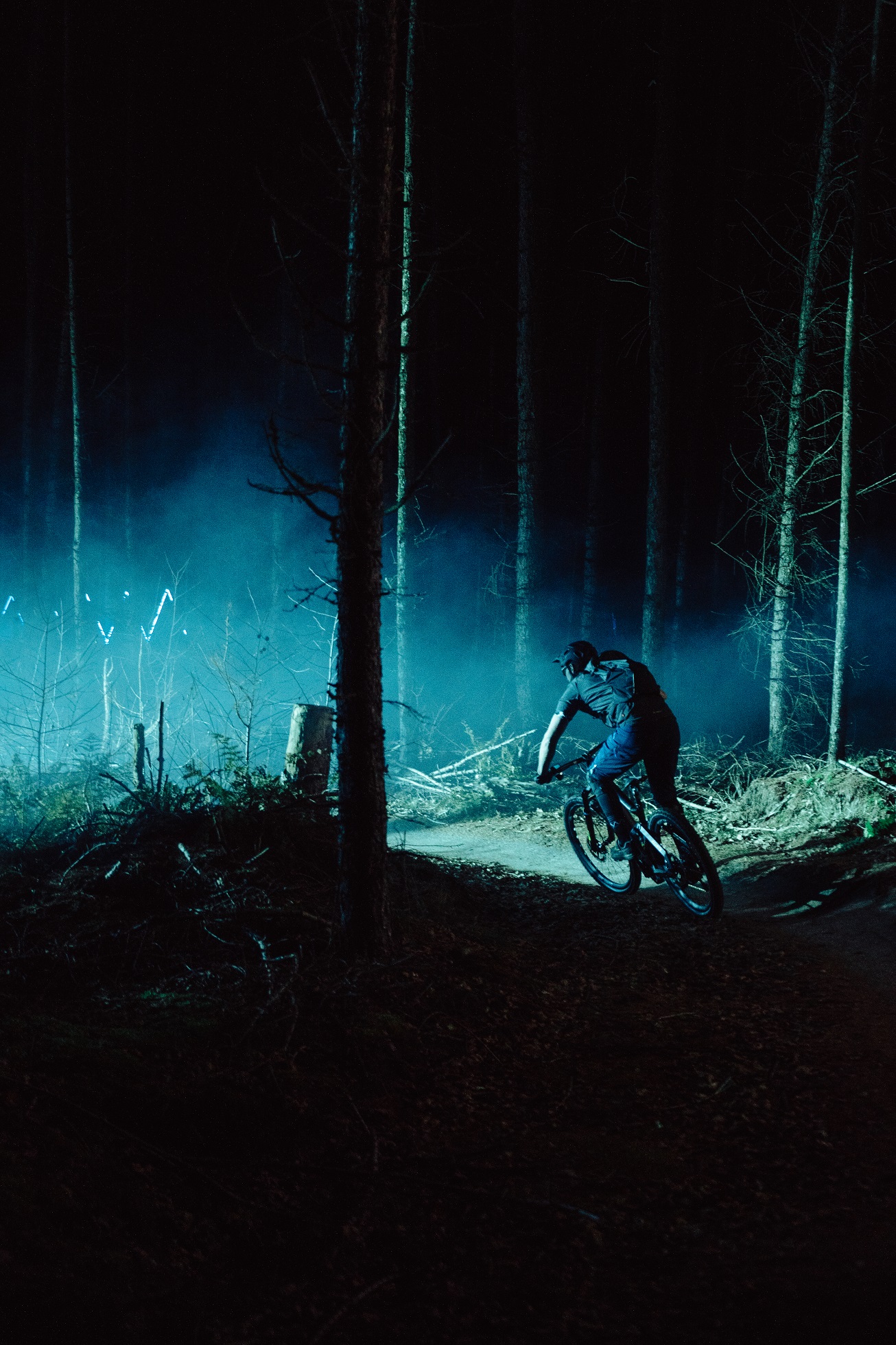 Silueta muže na horském kole v temném lese s modrými světly v pozadí