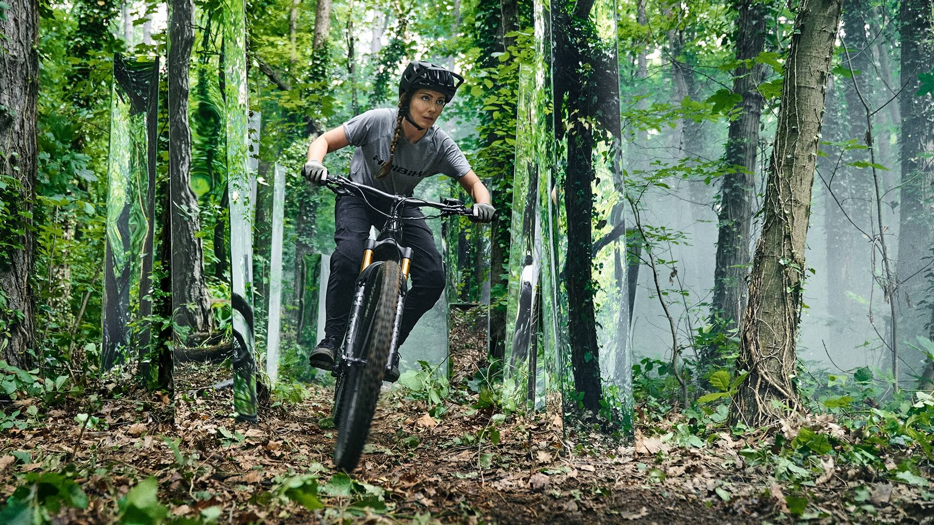 Celine cabalgando por un bosque futurista con espejos en su Haibike AllMtn 7 eMTB
