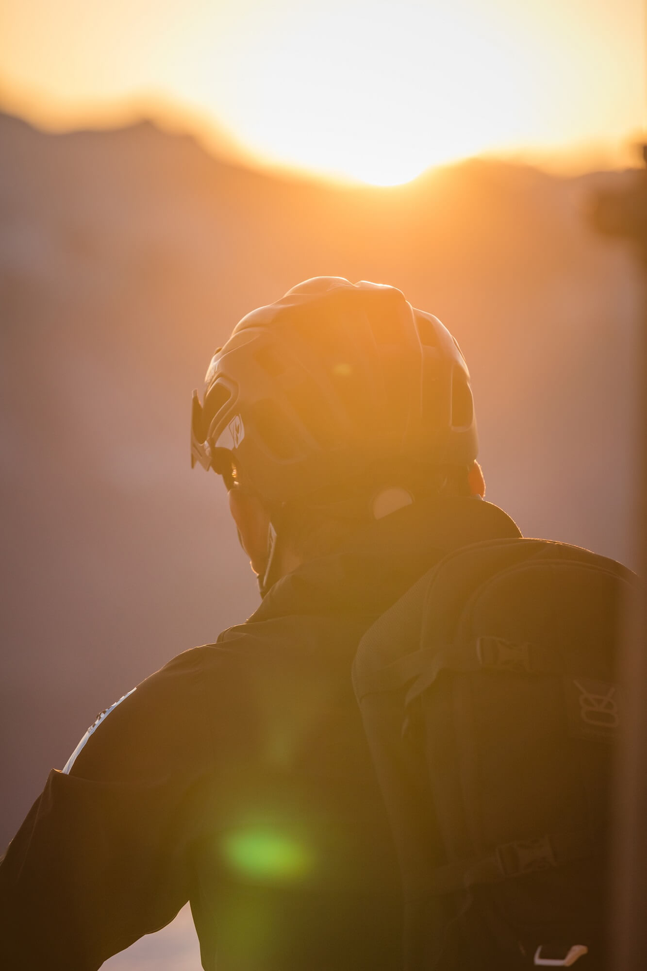Image portrait montrant le dos de Xavier Marovelli portant un casque avec le soleil du soir regardant à travers les montagnes en arrière-plan