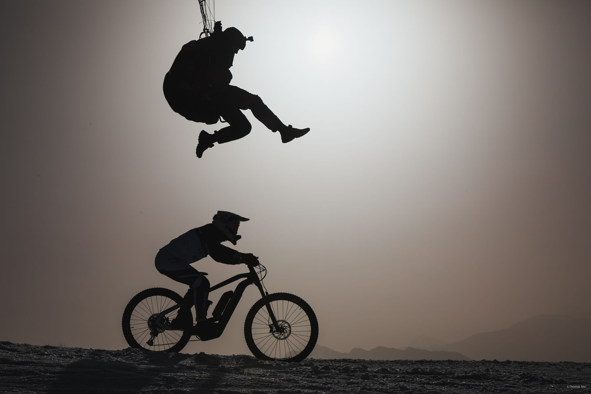 Silhouette de Tim Alongi volant avec son parachute au-dessus de Xavier Marovelli chevauchant son Haibike eMTB