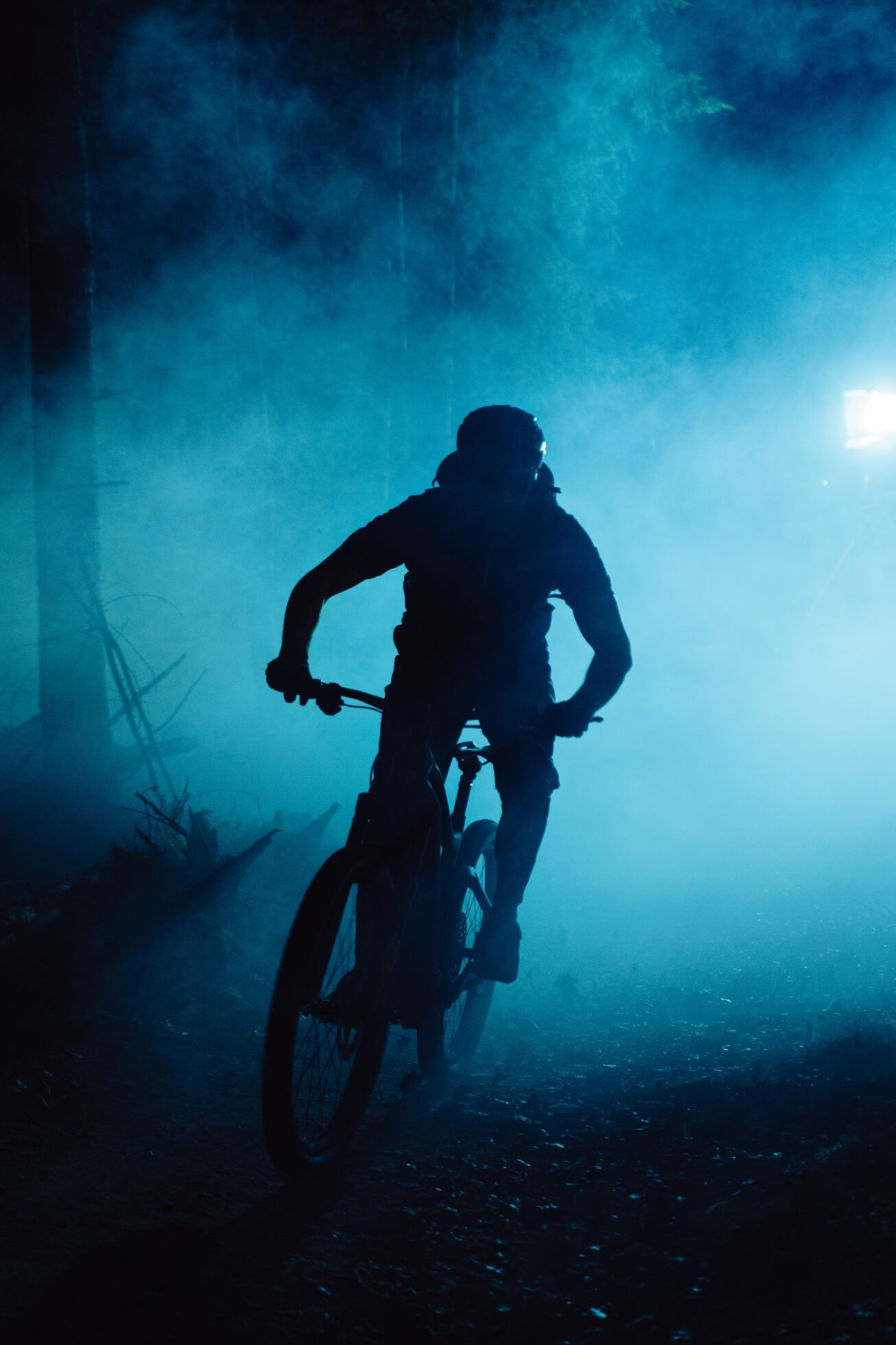 Silhouette of a man riding his mountain bike in a dark forest with blue lights in the background